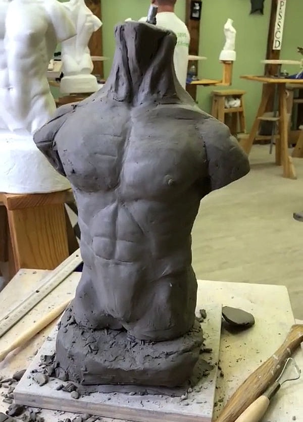 Clay sculpture of a male torso in progress.