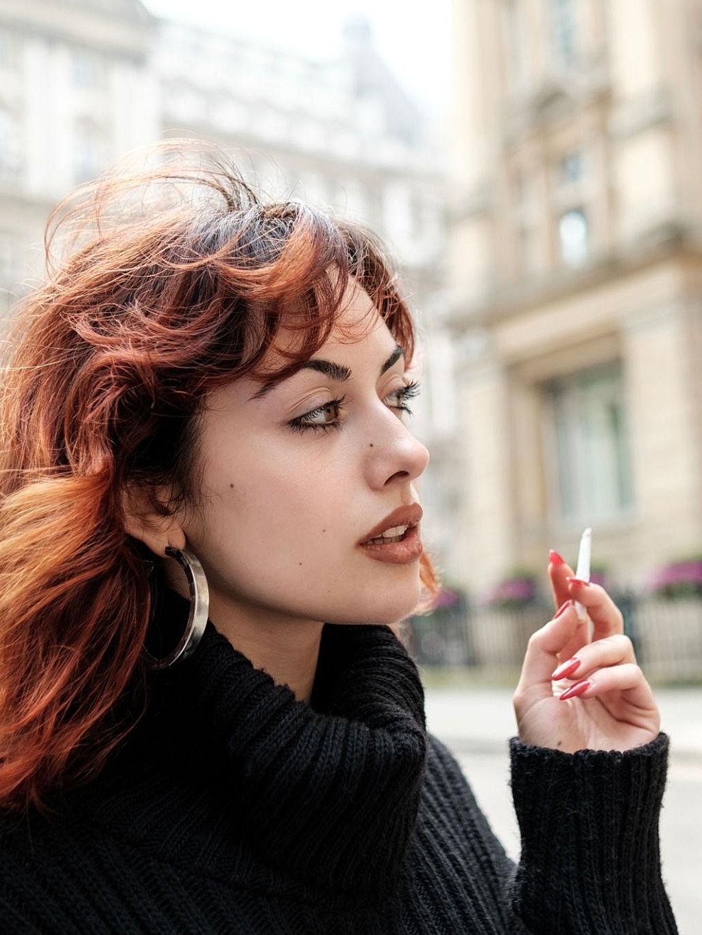 Woman with red hair holding a cigarette outdoors.