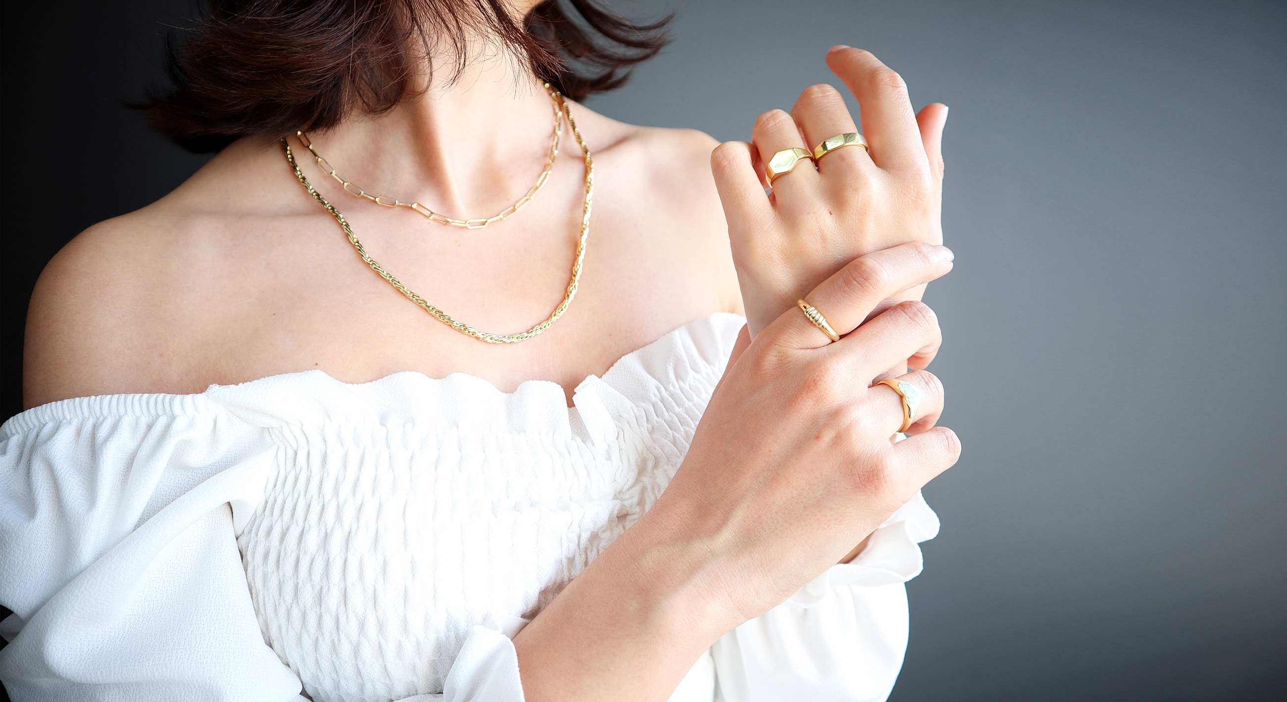 Model wearing elegant gold jewelry and white blouse.